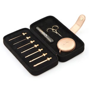 May include: A black, zippered case with a gold clasp, containing crochet hooks, scissors, a tape measure, and a wooden tool. The case is open, revealing the tools arranged on a black velvet interior.