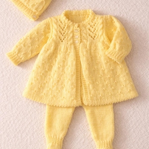 May include: A three-piece baby set in a soft yellow hue. The set includes a knitted hat, a long-sleeved cardigan with button closures, and matching footed pants. The cardigan features a decorative knit pattern around the neckline.