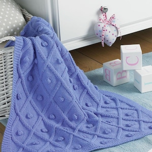 May include: A blue knitted baby blanket with a textured diamond pattern and small, raised circles. The blanket is lying on a light blue rug.