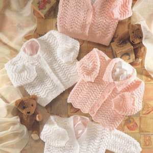May include: Four knitted baby cardigans in white and pink. Each has a scalloped edge and a satin lining. A teddy bear and a small toy block are in the background. The cardigans are in a variety of sizes.