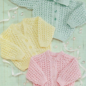 Peut inclure: Trois cardigans en tricot pour bébé dans différentes couleurs : bleu clair, jaune et rose. Chaque cardigan a une fermeture à boutons et un motif en dentelle.