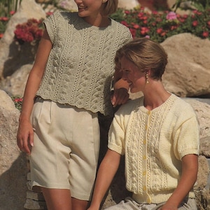May include: Two women in knitted outfits. One wears a light green sleeveless top and beige shorts. The other has a yellow short-sleeved cardigan and patterned trousers. Both tops feature a detailed knit pattern, ideal for spring or summer.