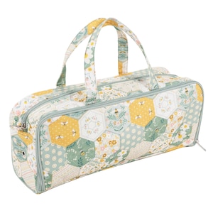 May include: A quilted, rectangular bag with a floral and bee pattern. The bag features a patchwork design with yellow, green, and white hexagonal shapes. It has two handles and a zipper closure, ideal for carrying craft supplies.