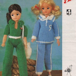 Pode incluir: Padrão de tricô para roupas de boneca. O padrão é para um macacão verde e um traje de marinheiro azul. O padrão é da marca de fio Emu, um fio de 4 fios.