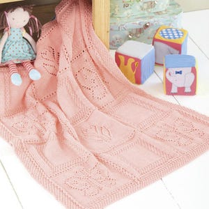 Könnte beinhalten: Eine rosa gestrickte Babydecke mit einem zarten Spitzenmuster. Die Decke ist aus weichem Garn gefertigt und zeigt verschiedene florale Motive.