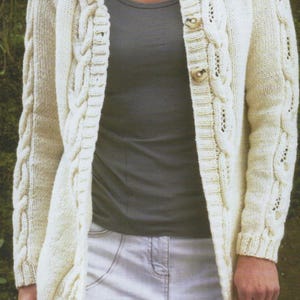 Peut inclure: Un cardigan blanc en tricot avec un motif en câble et une fermeture à boutons. Le cardigan a un col et des manches longues.