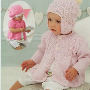 May include: A pink knitted baby cardigan with a button closure and a matching pink knitted hat with a white pom-pom. The hat has ear flaps.