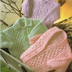 May include: Three knitted baby sweaters in different colours: light green, pink and lavender. Each sweater features a cable knit pattern.