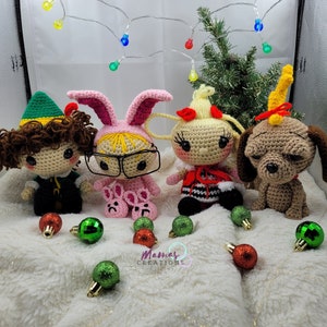 May include: Four crocheted Christmas characters: an elf, a bunny, a girl with blonde hair, and a dog. The characters are sitting on a white fluffy surface with green and red Christmas ornaments.