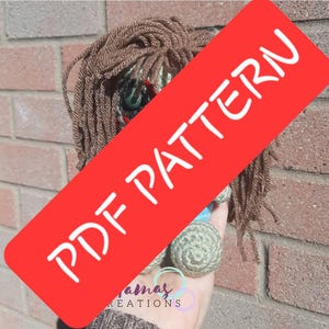 May include: A handmade doll with brown yarn hair and green button eyes. The doll has a red banner across it that says "PDF PATTERN" in white letters. The doll is held in a hand.