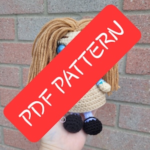 May include: A handmade crochet doll with long, light brown yarn hair and a beige dress. The doll has black shoes and blue eyes. A red banner with the text "PDF PATTERN" is across the image.