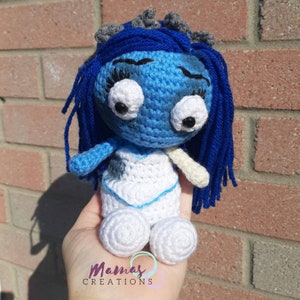 Peut inclure: Une poupée en crochet bleue avec des yeux blancs et une robe blanche. La poupée a de longs cheveux bleus et des pieds en crochet blancs.