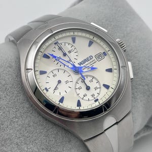 May include: A silver-toned stainless steel chronograph watch with a white dial, blue hands, and blue hour markers. The watch face features the text WIRED, CHRONOGRAPH, WATER RESIST 10 BAR, and a date window at the three o'clock position. It has three sub-dials.