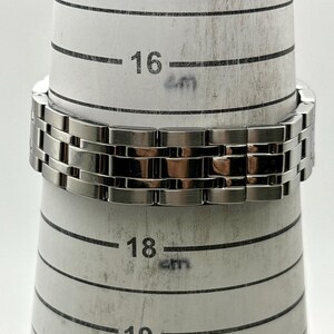 May include: A silver-toned metal bracelet is wrapped around a ring sizer. The bracelet is made of rectangular links. The ring sizer has measurements in centimeters, with the bracelet resting at the 16 cm mark.