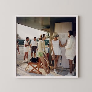 May include: A framed photograph of a group of people at a tennis court. Several people are wearing tennis attire, including white shorts and skirts. A woman wears a straw hat and a white dress. Tennis rackets are visible.