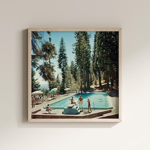 May include: A framed print of a vintage photograph depicting a swimming pool scene. The pool is surrounded by people, trees, and umbrellas. The image has a retro aesthetic, with a focus on leisure and outdoor recreation.