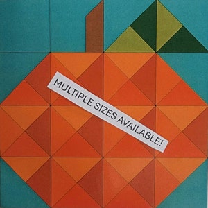 May include: A geometric pumpkin quilt block pattern in orange, brown, and green. The block is surrounded by a teal border. The text "MULTIPLE SIZES AVAILABLE!" is on a white label.