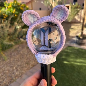 May include: A black and clear light stick with a purple and white crocheted cover. The cover has two ear-shaped accents. The light stick has a logo in the center.