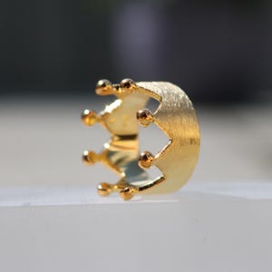 May include: A gold crown ring with a brushed finish. The ring is designed with a simple crown shape and five points.