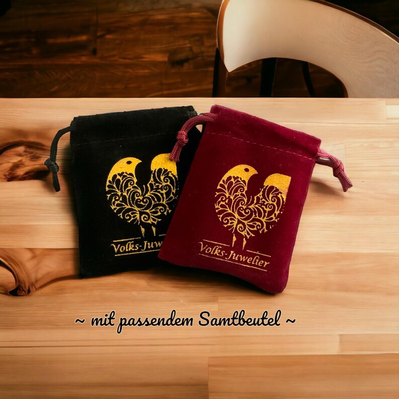May include: Two small velvet pouches with drawstrings. The pouches are red and black and feature a gold bird design with the text "Volks-Juwelier" printed on them.