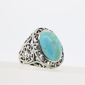 May include: A silver ring featuring a large, oval-shaped turquoise stone with natural brown veining. The band is crafted with intricate, openwork scroll patterns that surround the central stone, creating a detailed and ornate metal frame.