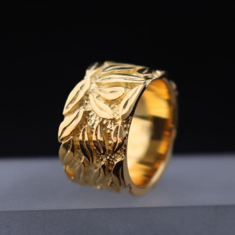 May include: A gold ring with a textured design of leaves. The ring is wide and has a polished finish.