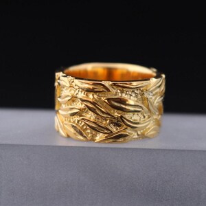 May include: A gold ring with a textured design of interwoven leaves and swirls.