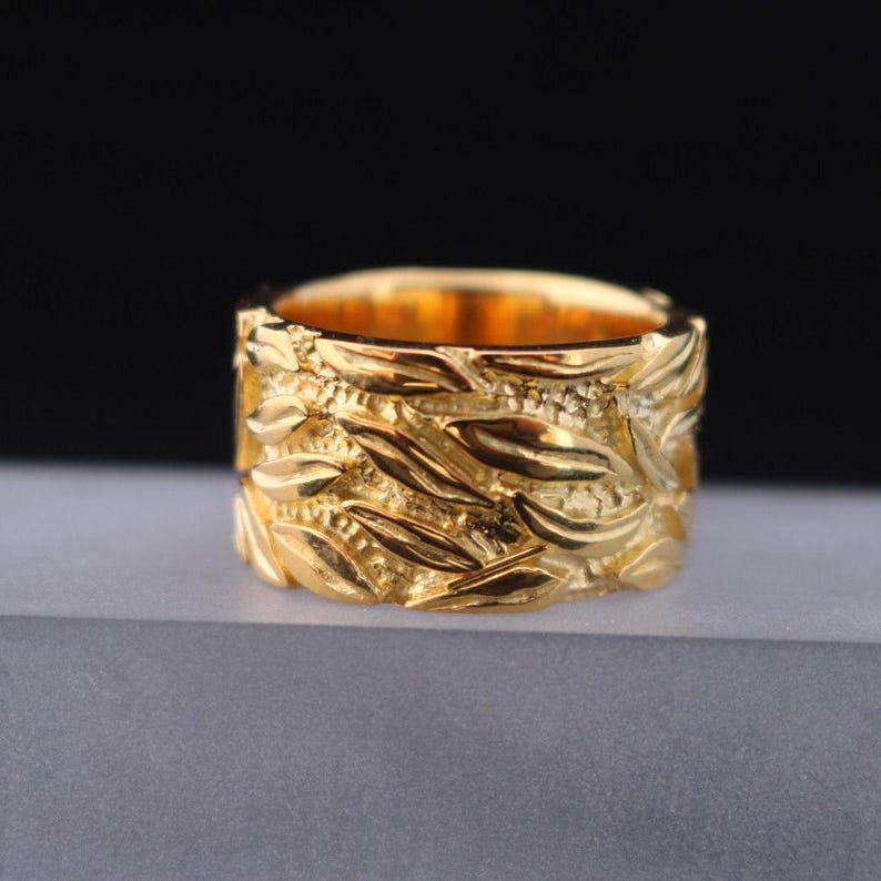 May include: A gold ring with a textured design of interwoven leaves and swirls.