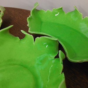 May include: Three green ceramic bowls with an irregular, wavy edge. The bowls are made of a smooth, glossy material and have a light green color.
