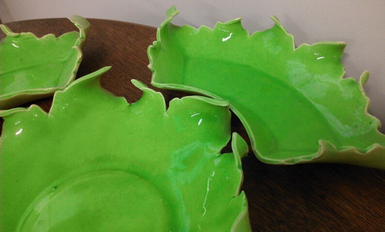 May include: Three green ceramic bowls with an irregular, wavy edge. The bowls are made of a smooth, glossy material and have a light green color.