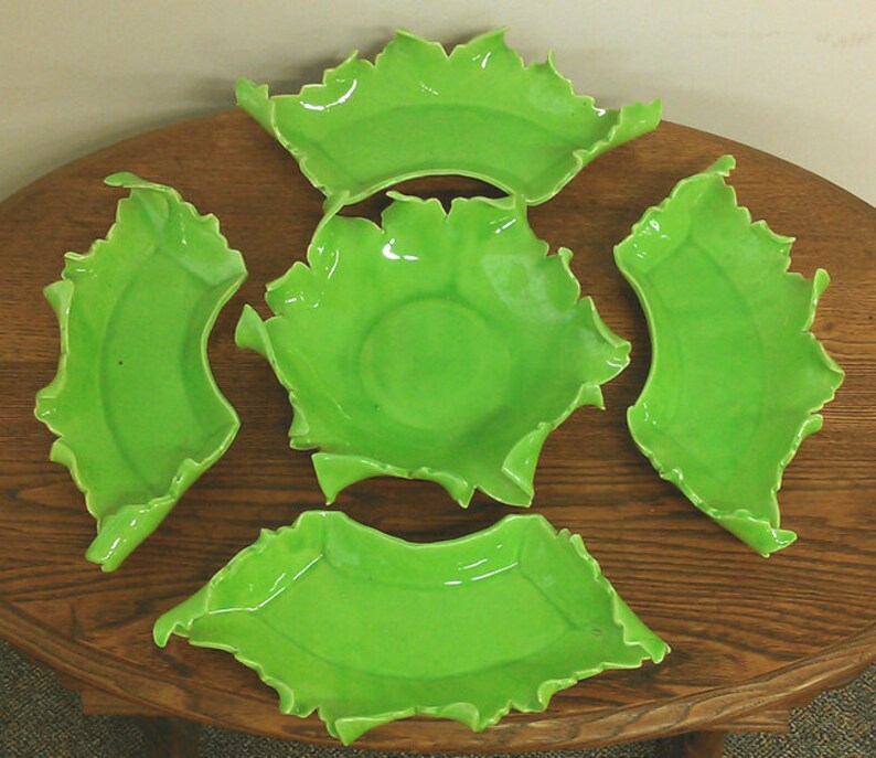 May include: Set of five green ceramic bowls with a unique, ruffled edge design. The bowls are arranged on a wooden surface.