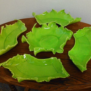 May include: Five green ceramic bowls with scalloped edges. The bowls are arranged on a wooden table.