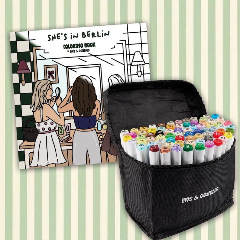 Op de afbeelding: Een zwarte draagtas vol kleurrijke stiften naast een kleurboek met de titel "She's in Berlin". Het kleurboek toont een zwart-wit illustratie van twee vrouwen voor een spiegel. De tas heeft de tekst "UNS & GOEBNS."