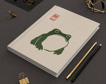 Cuaderno de tapa dura con diseño de rana japonesa, inspirado en el arte minimalista de Matsumoto Hoji, con ilustraciones de tinta y líneas.