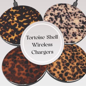 Puede incluir: Cuatro cargadores inalámbricos redondos con patrones de caparazón de tortuga en tonos marrón, beige y crema. Los cargadores tienen un diseño elegante y un cable negro. El texto "Tortoise Shell Wireless Chargers" está presente.