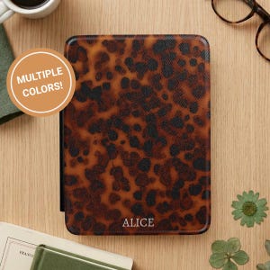 Könnte beinhalten: Eine braun-schwarz gemusterte E-Reader-Hülle mit dem weißen Namen "ALICE". Die Hülle hat ein Schildpatt-Design. Ein runder Aufkleber oben links lautet "MEHRERE FARBEN!".