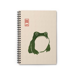 Peut inclure: Cahier à spirales avec une couverture beige. Il présente une illustration de grenouille verte avec une grande bouche ouverte, dans un style minimaliste. Un carré rouge avec du texte japonais est dans le coin supérieur gauche.