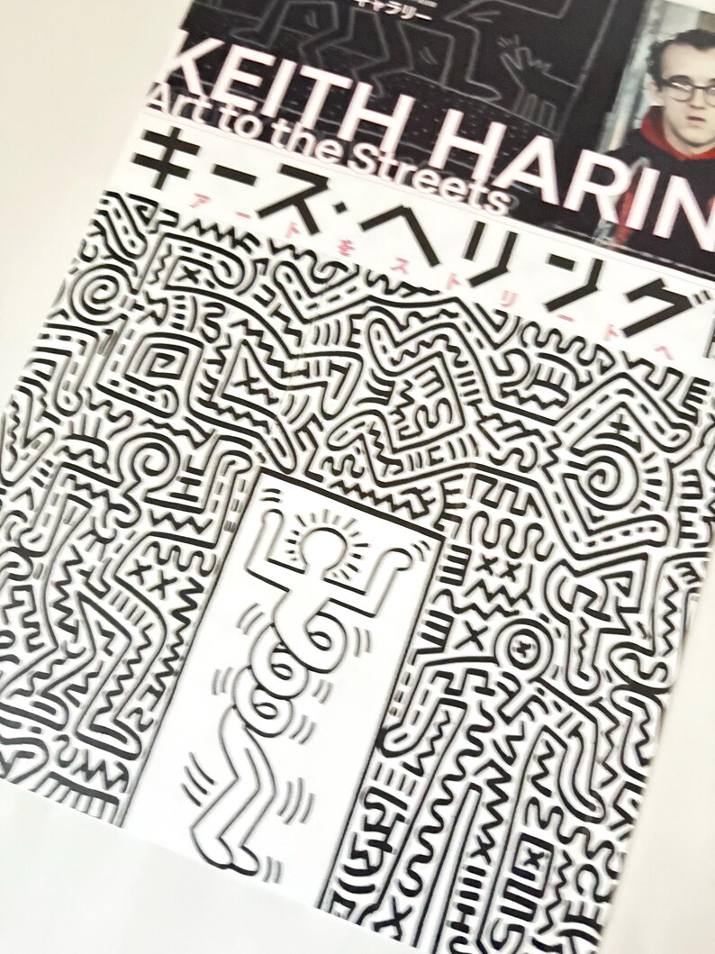 May include: A black and white book cover with the title "Keith Haring Art to the Streets" in white text. The cover features a black and white illustration of a stick figure dancing in a black and white abstract pattern.