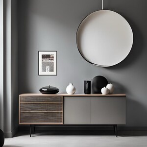 May include: A gray dresser with three drawers and two cabinet doors. The dresser has black metal legs. There is a framed black and white print of a Keith Haring artwork on the wall above the dresser. There is a round white ceiling light fixture hanging above the dresser. There are three white ceramic vases and a black ceramic bowl on top of the dresser.