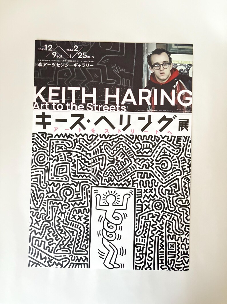 May include: A black and white poster advertising an exhibit of Keith Haring's art. The poster features a black and white illustration of a person with a halo and a series of circles around their torso. The text on the poster reads "Keith Haring Art to the Streets" and "キース・ヘリング展".