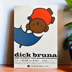 Puede incluir: Un póster que anuncia una exposición de las obras de Dick Bruna para libros ilustrados para niños. El póster presenta un oso marrón con un sombrero rojo y sosteniendo un paraguas azul. El texto en el póster dice "dick bruna zijn werken voor prentenboeken" y "ブルーナ絵本展 2024年4月24日(水)~5月13日(月) 大丸ミュージアム(梅田) DAIMARU".