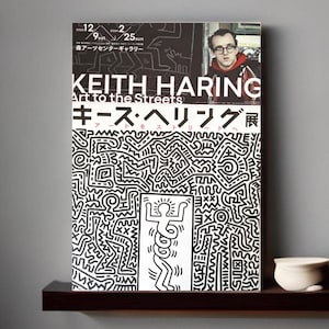 May include: A black and white poster with a graphic design of a stick figure with a sun above its head. The poster is for a Keith Haring exhibition titled "Art to the Streets" and features the text "Keith Haring" and "Art to the Streets" in large, bold letters. The poster also includes the text "キース・ヘリング展" in Japanese.