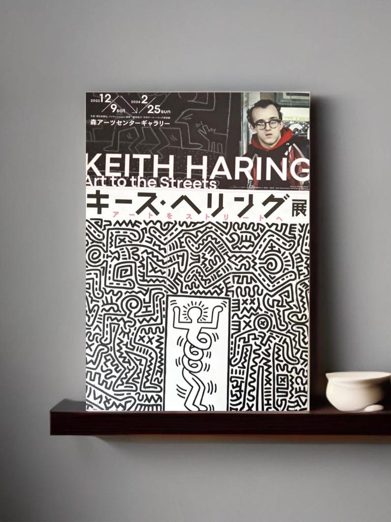 May include: A black and white poster with a graphic design of a stick figure with a sun above its head. The poster is for a Keith Haring exhibition titled "Art to the Streets" and features the text "Keith Haring" and "Art to the Streets" in large, bold letters. The poster also includes the text "キース・ヘリング展" in Japanese.