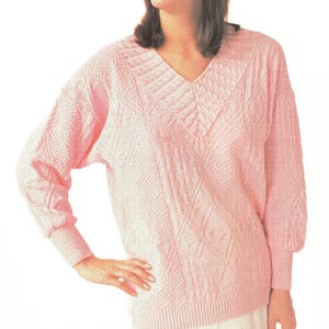 May include: A pink knitted sweater with a v-neck and a cable knit pattern.