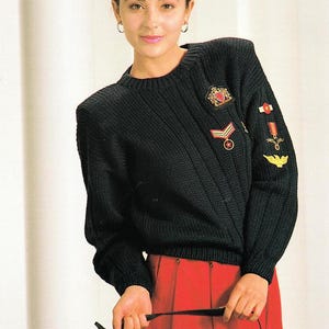 Könnte beinhalten: Ein schwarzer Strickpullover mit verschiedenen goldenen und roten Stickereien auf der Vorderseite und dem Ärmel. Der Pullover hat eine gerippte Struktur und einen Rundhalsausschnitt.