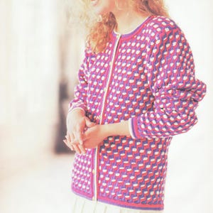 May include: A pink and white knitted cardigan with a geometric pattern. The cardigan has a button-up front and long sleeves.