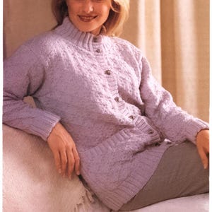 以下が含まれることがあります： ハイネックとボタン留めが特徴のラベンダー色のニットカーディガン。カーディガンはテクスチャのあるパターンで、人が着用している様子が写っています。