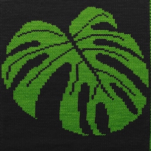 Könnte beinhalten: Gestrickter Stoff mit einem großen, stilisierten grünen Monstera-Blatt-Design auf schwarzem Hintergrund. Das Blatt hat komplizierte Details und ein strukturiertes Aussehen, das ein botanisches Thema zeigt.