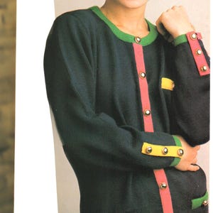 May include: A navy blue cardigan with a green, pink and yellow trim. The cardigan has gold buttons and a pocket on the front.