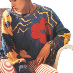 May include: A blue knitted sweater with a red flower, yellow wavy lines, and a yellow and blue geometric pattern.